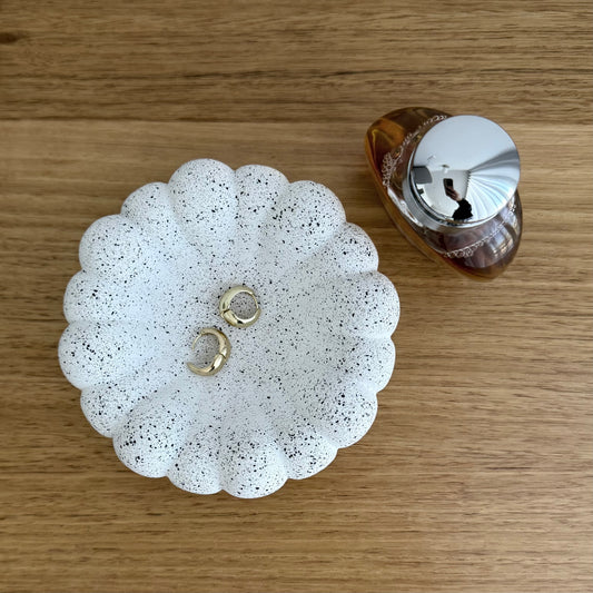Overhead view of Cove decorative bowl in textured stone-inspired finish styled on timber table with jewellery and a perfume bottle.