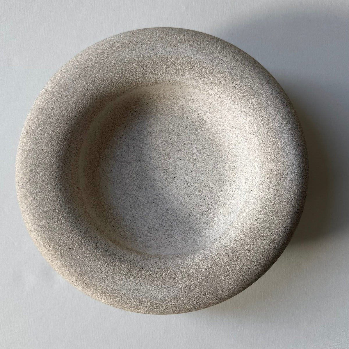 An overhead view of the handcrafted Halo Footed Bowl featuring a warm natural stone finish and rounded sculptural feet.