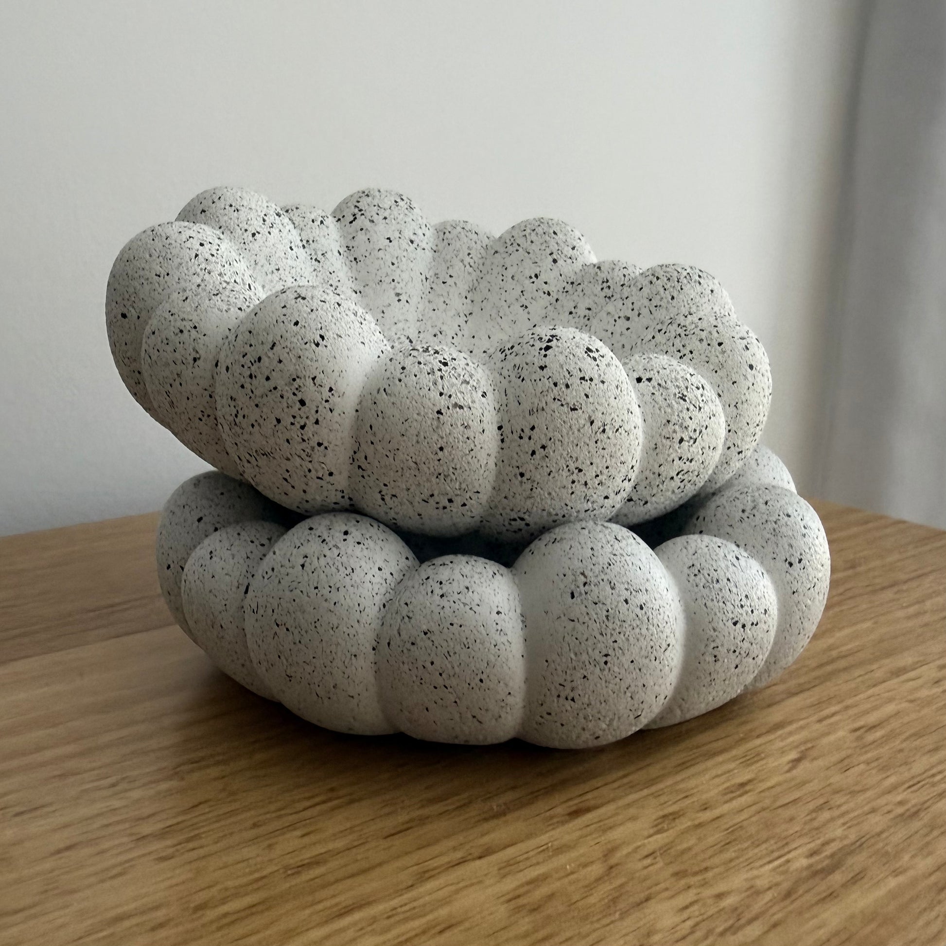 Two stacked Cove decorative bowls in textured stone-inspired finish styled on timber table with jewellery and a perfume bottle.