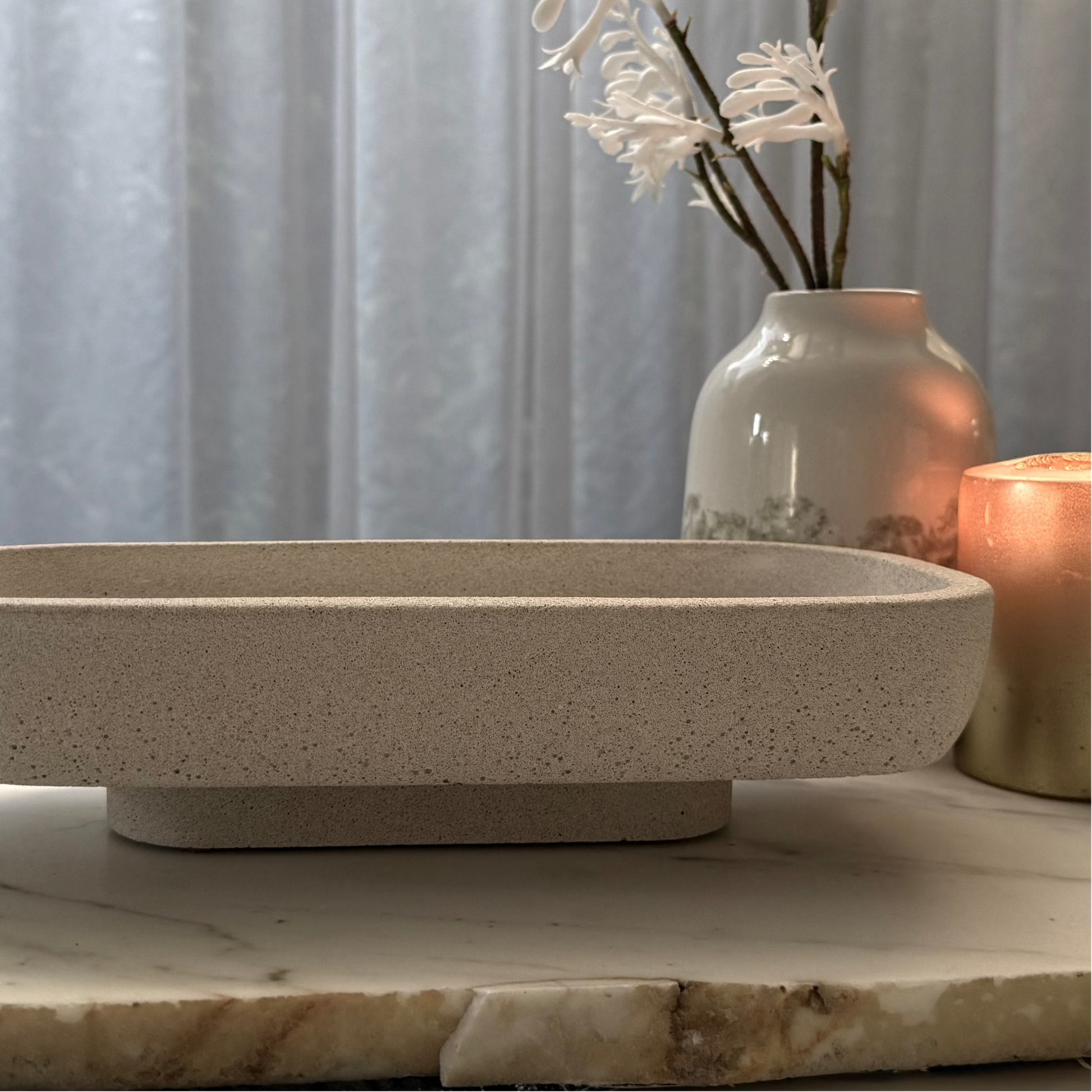 Handcrafted Monolith pedestal featuring a solid yet minimalist rectangular form with a natural stone-inspired finish and rounded corners. Styled with ceramic vase and candle.