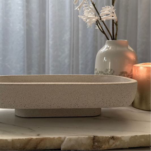 Handcrafted Monolith pedestal featuring a solid yet minimalist rectangular form with a natural stone-inspired finish and rounded corners. Styled with ceramic vase and candle.