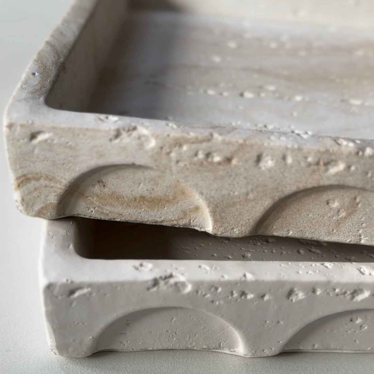 A close up of two handcrafted Portico trayss highlighting the detail of their distinctive arch profile and textured stone-inspired finishes.