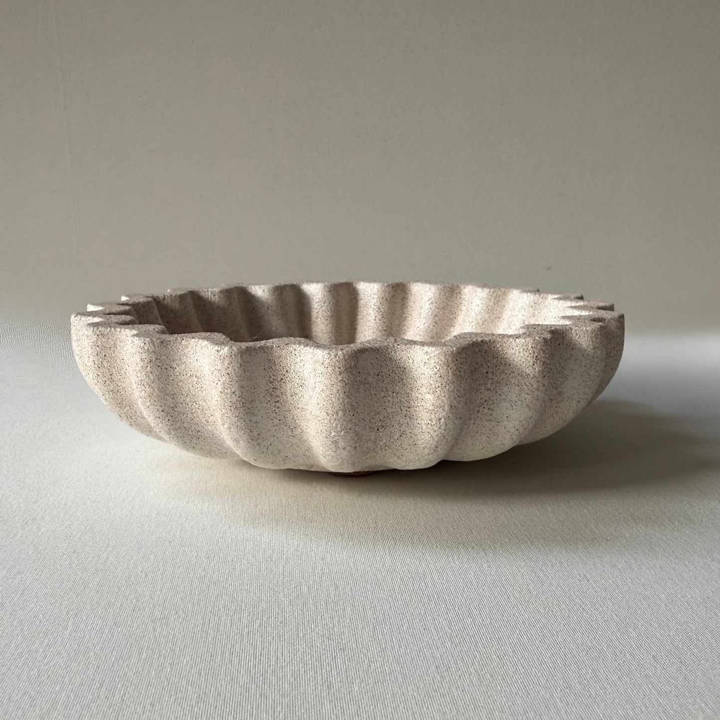 Side profile of handcrafted Ripple Bowl, showcasing it's sculptural rippled edges and textured stone-inspired finish.