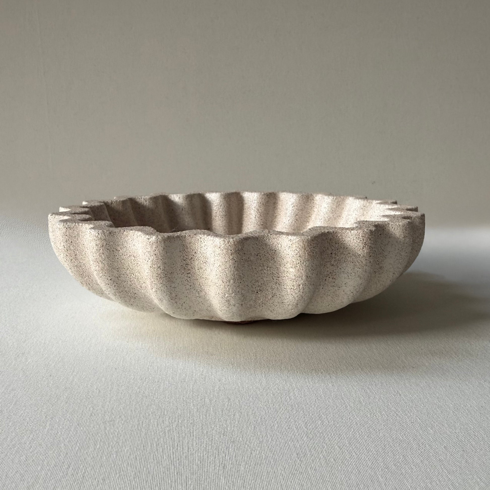 Side profile of handcrafted Ripple Bowl, showcasing it's sculptural rippled edges and textured stone-inspired finish.