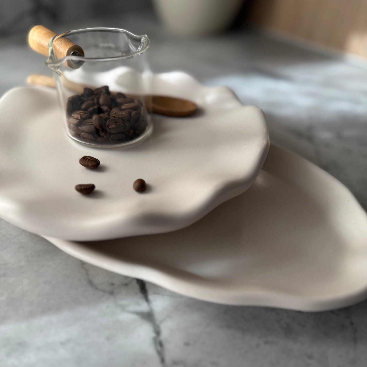 Two stacked handcrafted Shore Trays in smooth natural stone-inspired finish styled with glass coffee server and coffee beans.