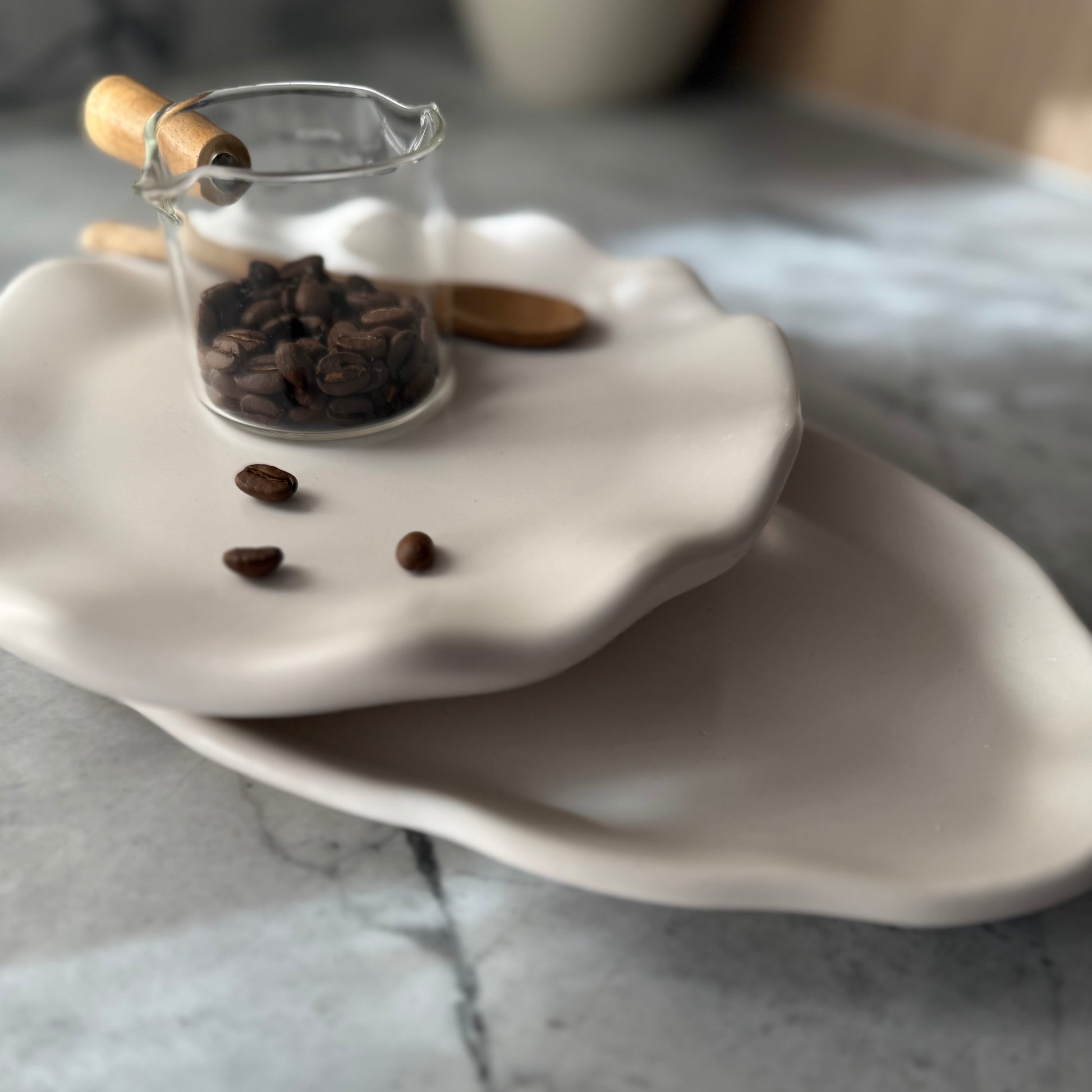 Two stacked handcrafted Shore Trays in smooth natural stone-inspired finish styled with glass coffee server and coffee beans.
